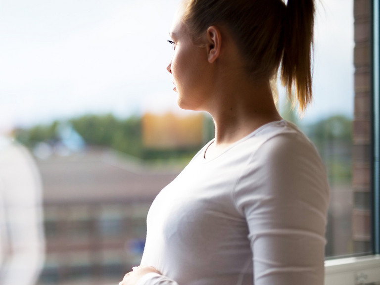 Frau hält Hand auf Bauch und schaut aus dem Fenster Frau hält Hand auf Bauch und schaut aus dem Fenster