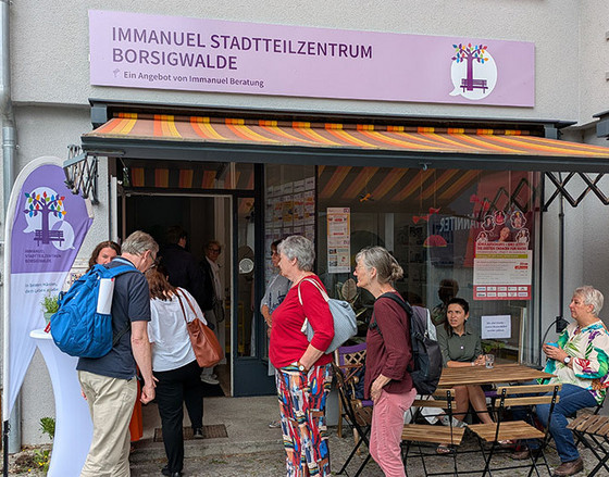 Mehrere Personen stehen oder sitzen auf einer Sitzbank vor dem geöffneten Immanuel Stadtteilzentrum Borsigwalde und unterhalten sich Mehrere Personen stehen oder sitzen auf einer Sitzbank vor dem geöffneten Immanuel Stadtteilzentrum Borsigwalde und unterhalten sich